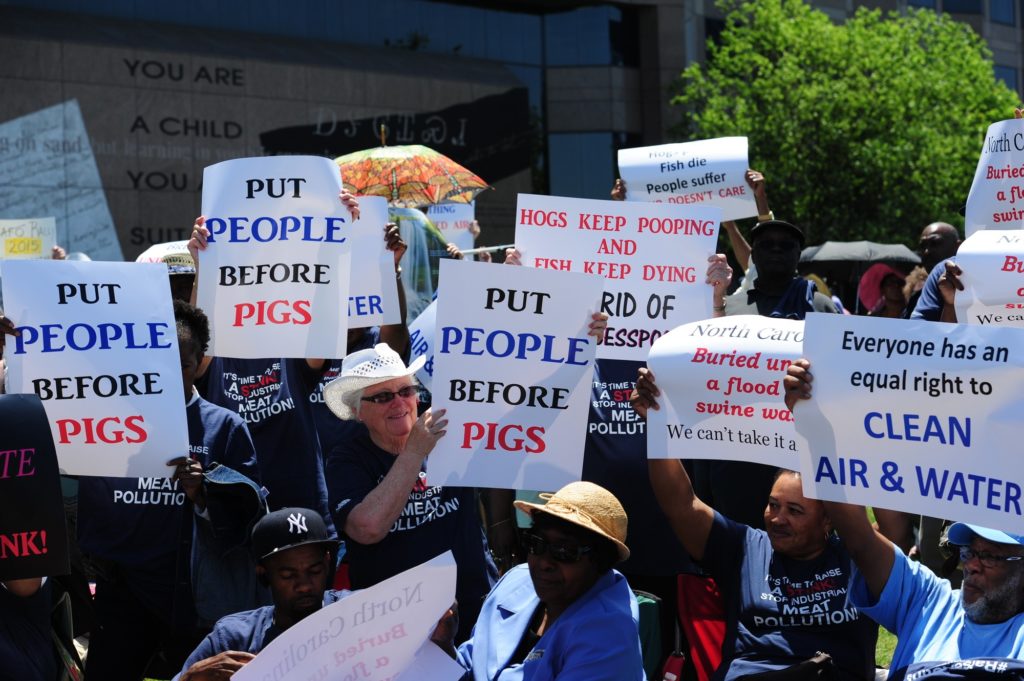 Multiple people holding signs saying "put people before pigs". 