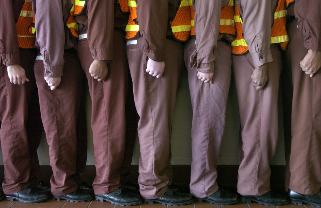 Six prisoners in their uniforms lined up in a line facing sideways. 