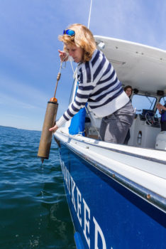 Casco Baykeeper Ivy Frignoca takes a water sample from a boat.