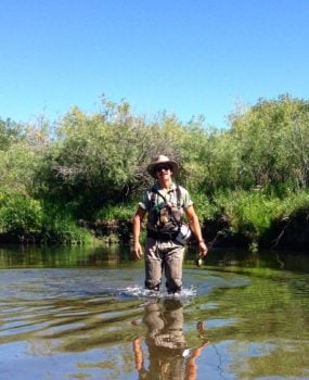 Alto Missouri Waterkeeper Guy Alsentzer se encuentra en el agua hasta las rodillas en un río con árboles al fondo.